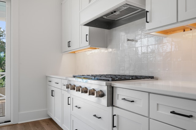 kitchen featuring stainless steel gas stovetop, premium range hood, white cabinets, dark hardwood / wood-style floors, and decorative backsplash