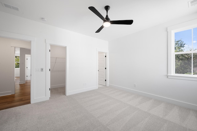 unfurnished bedroom featuring a spacious closet, a closet, ceiling fan, and light carpet