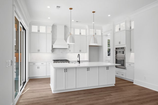 kitchen featuring premium range hood, white cabinetry, an island with sink, and appliances with stainless steel finishes