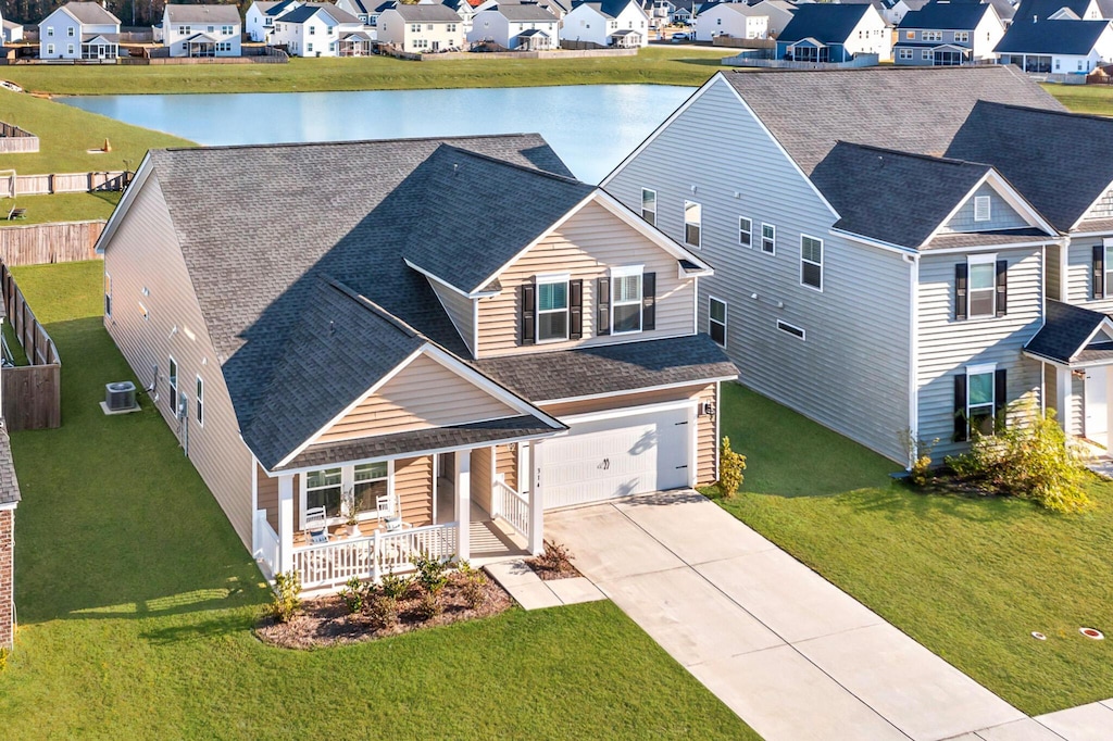 view of front of home featuring a garage, a water view, a front lawn, central AC unit, and covered porch