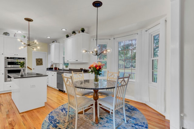 kitchen featuring light wood-type flooring, stainless steel appliances, white cabinetry, and an inviting chandelier