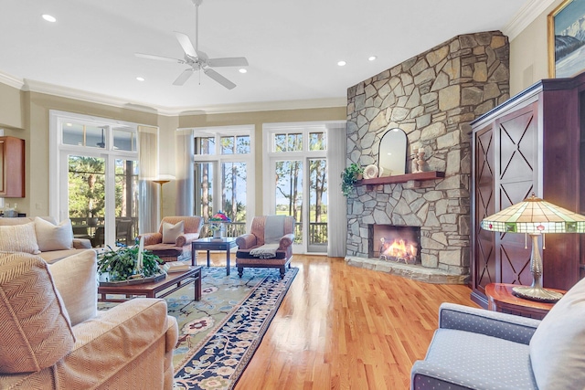 living room with light wood-type flooring, crown molding, ceiling fan, a stone fireplace, and french doors