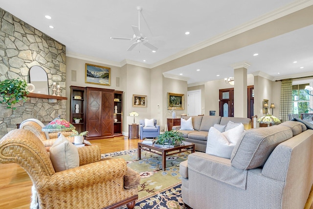 living room featuring light wood-type flooring, crown molding, ceiling fan, and a stone fireplace