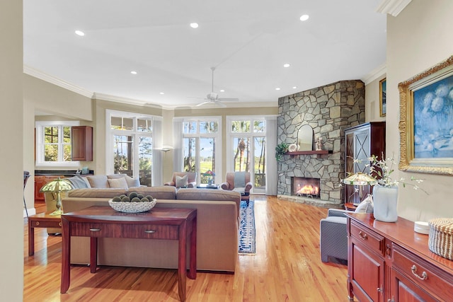 living room with light hardwood / wood-style flooring, ceiling fan, ornamental molding, and a stone fireplace