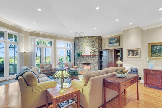 living room featuring light hardwood / wood-style flooring, ceiling fan, ornamental molding, and a stone fireplace