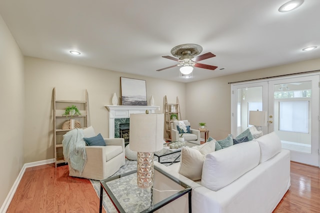 living room with ceiling fan, light wood-type flooring, french doors, and a fireplace