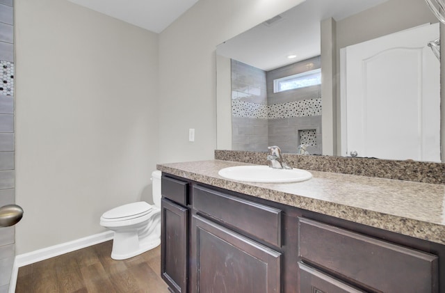 bathroom featuring toilet, hardwood / wood-style flooring, tiled shower, and vanity