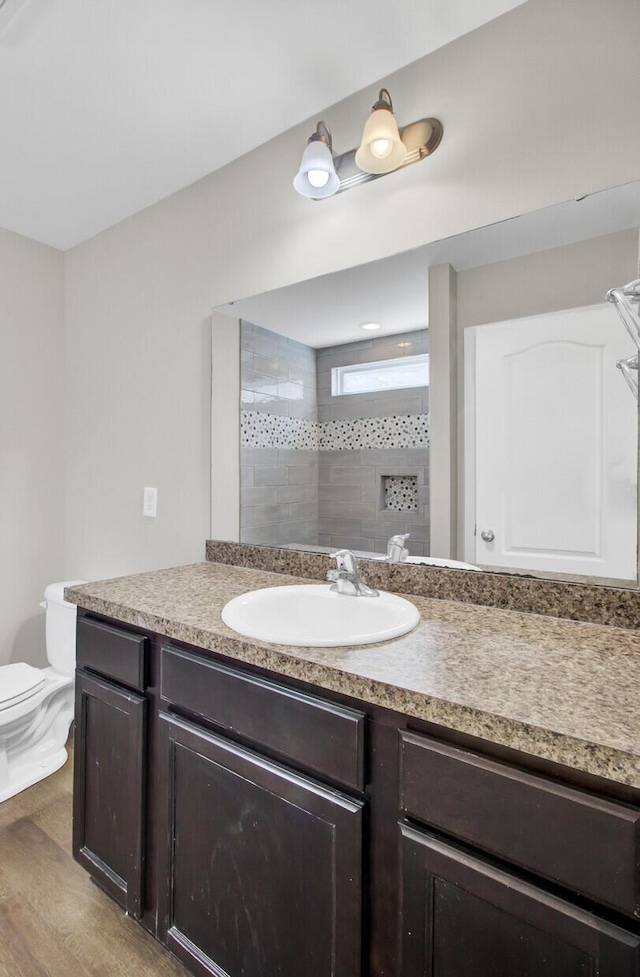 bathroom featuring tiled shower, toilet, vanity, and hardwood / wood-style flooring