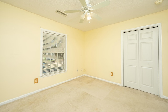 unfurnished bedroom featuring ceiling fan, light colored carpet, a closet, and a textured ceiling