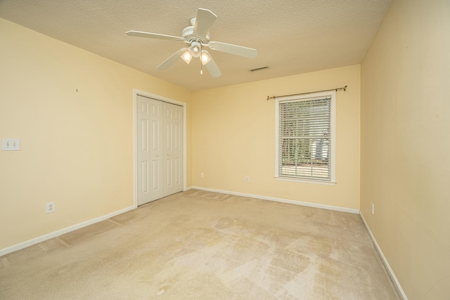 unfurnished bedroom featuring ceiling fan, a closet, light carpet, and a textured ceiling