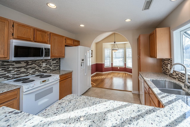 kitchen with sink, light stone counters, decorative light fixtures, a textured ceiling, and white appliances