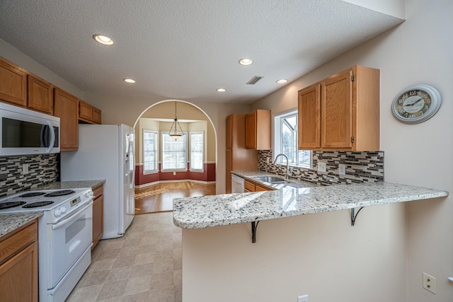 kitchen featuring a breakfast bar, sink, light stone counters, kitchen peninsula, and white appliances