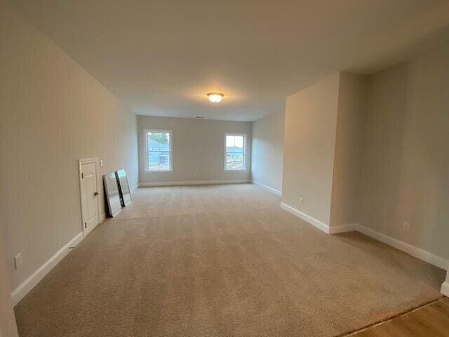 spare room featuring light colored carpet and baseboards