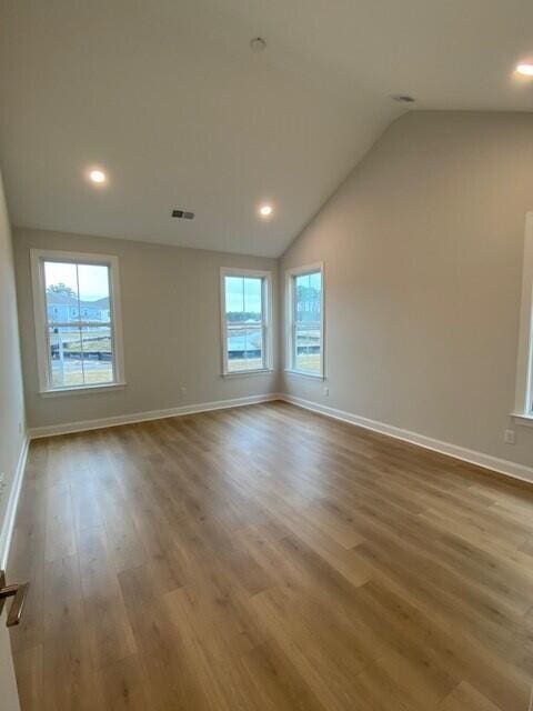 unfurnished room with lofted ceiling, recessed lighting, wood finished floors, visible vents, and baseboards