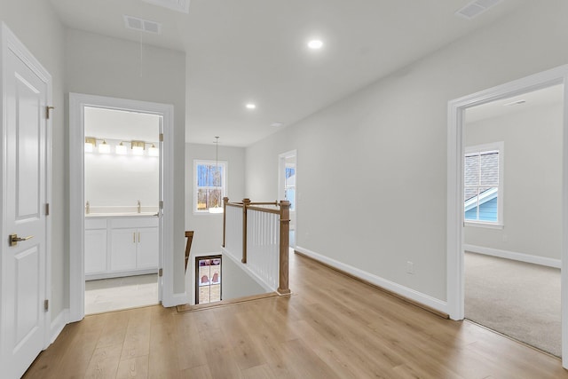 hallway featuring attic access, visible vents, light wood finished floors, and an upstairs landing