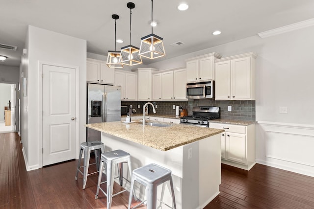 kitchen with white cabinetry, sink, dark wood-type flooring, stainless steel appliances, and a kitchen island with sink