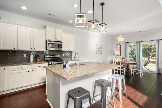 kitchen with hanging light fixtures, appliances with stainless steel finishes, dark hardwood / wood-style flooring, and a kitchen island with sink