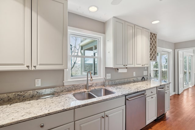 kitchen with white cabinets, dishwasher, light wood-style flooring, light stone counters, and a sink