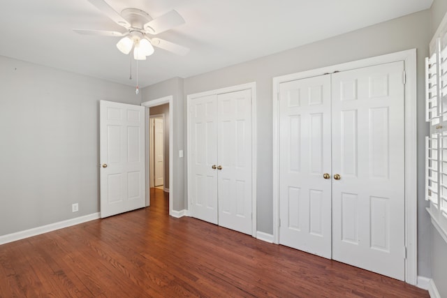 unfurnished bedroom featuring ceiling fan, wood finished floors, two closets, and baseboards