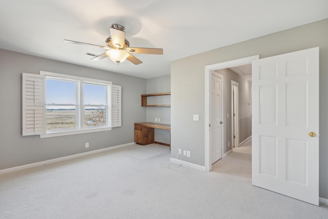 unfurnished bedroom featuring built in desk, visible vents, a ceiling fan, light carpet, and baseboards