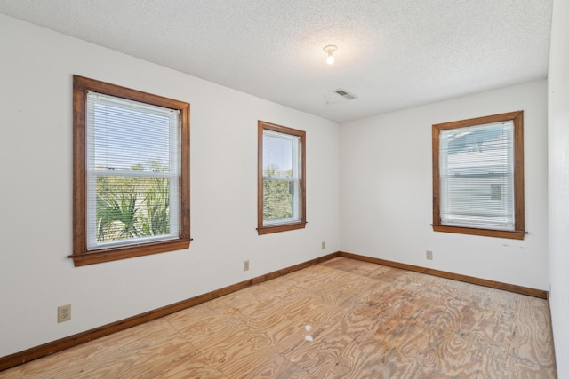 empty room featuring visible vents, a textured ceiling, and baseboards