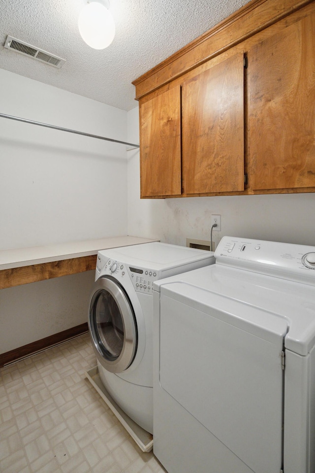 clothes washing area featuring cabinet space, baseboards, visible vents, a textured ceiling, and washer and dryer