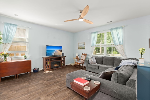 living room featuring a ceiling fan, wood finished floors, visible vents, baseboards, and a lit fireplace