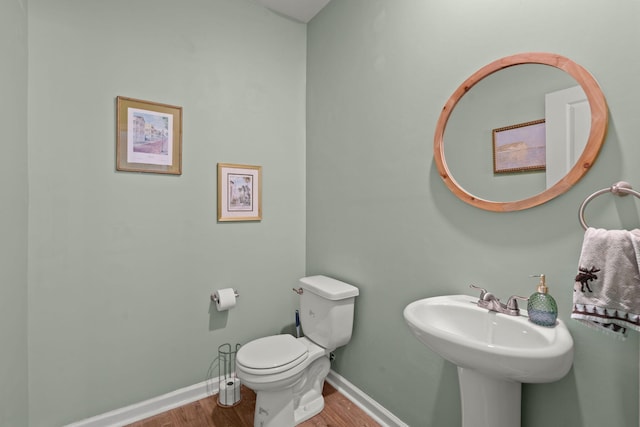 half bath with a sink, baseboards, toilet, and wood finished floors