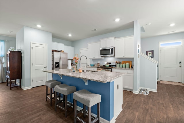 kitchen featuring light stone countertops, a breakfast bar, dark wood-type flooring, white cabinets, and appliances with stainless steel finishes