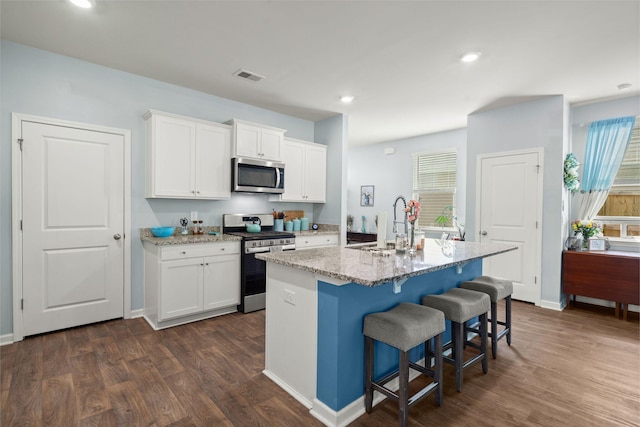 kitchen with visible vents, a sink, light stone counters, dark wood finished floors, and appliances with stainless steel finishes