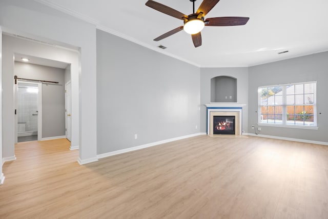 unfurnished living room featuring crown molding, light wood-type flooring, ceiling fan, and a barn door