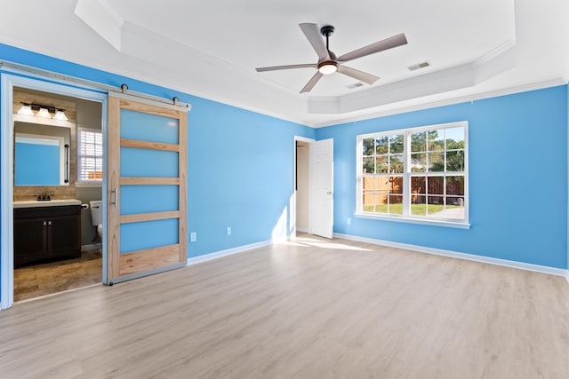 unfurnished bedroom featuring light hardwood / wood-style floors, ceiling fan, a raised ceiling, and a barn door