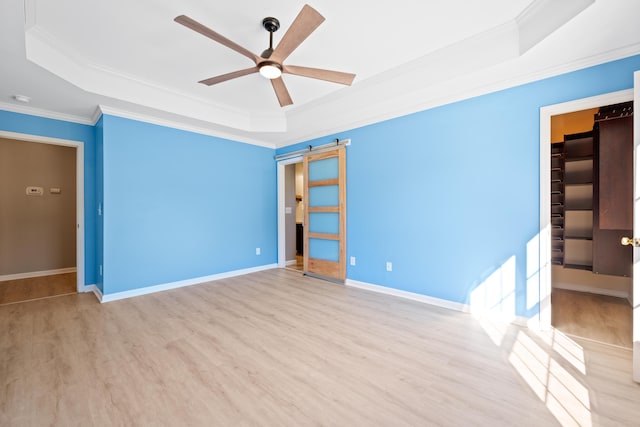 empty room with ceiling fan, a tray ceiling, ornamental molding, and light wood-type flooring