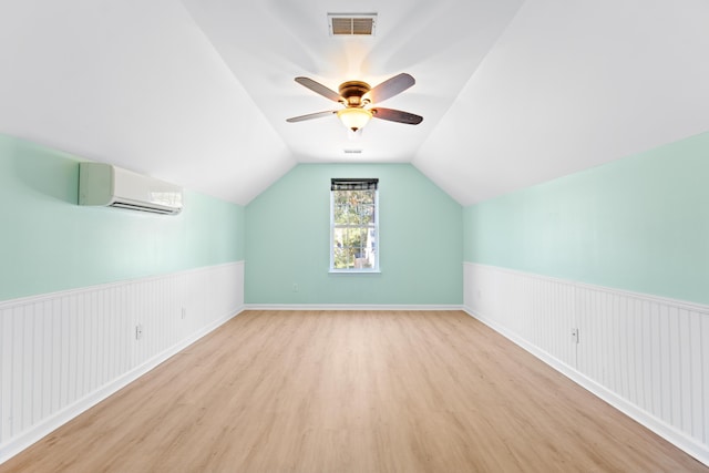 additional living space with a wall mounted AC, light hardwood / wood-style flooring, vaulted ceiling, and ceiling fan