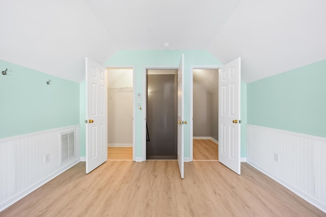 unfurnished bedroom with a walk in closet, a closet, lofted ceiling, and light wood-type flooring