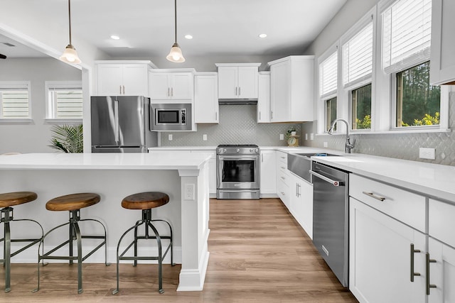 kitchen with decorative backsplash, a breakfast bar, stainless steel appliances, white cabinetry, and hanging light fixtures