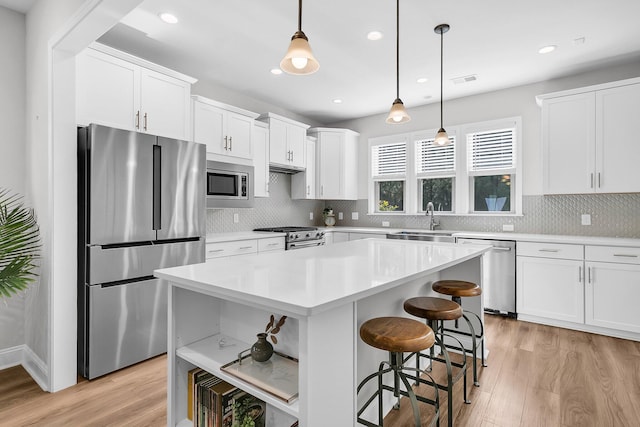 kitchen featuring a kitchen island, white cabinetry, stainless steel appliances, and hanging light fixtures