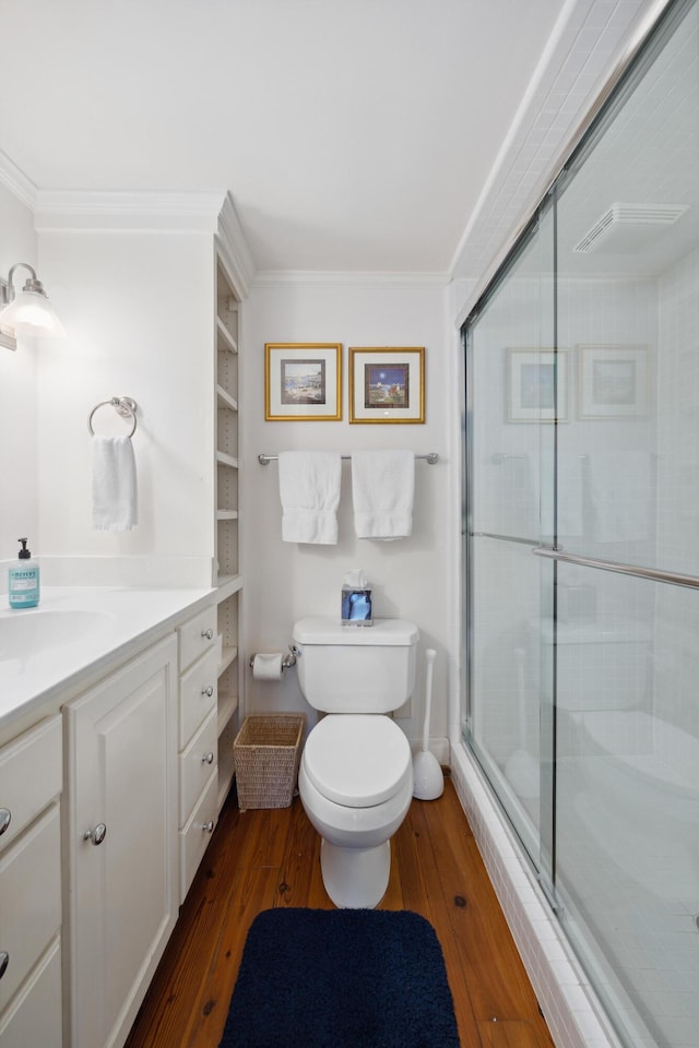 bathroom featuring toilet, a shower with shower door, wood-type flooring, ornamental molding, and vanity