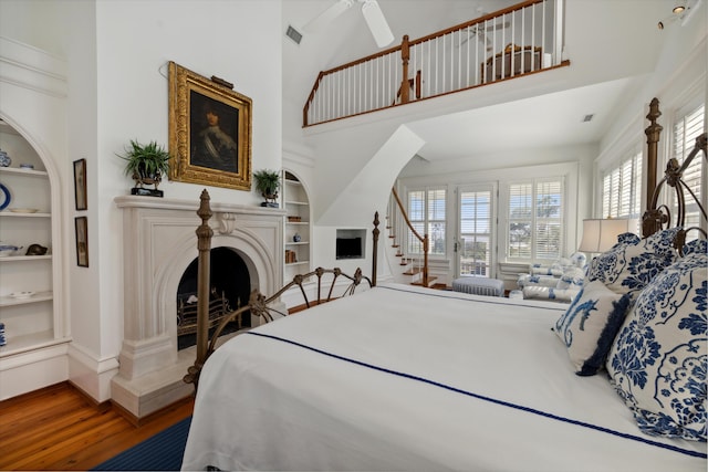 bedroom featuring a towering ceiling, multiple windows, hardwood / wood-style flooring, and ceiling fan