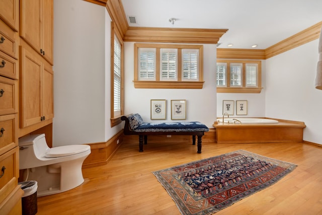 bathroom with toilet, wood-type flooring, ornamental molding, and a tub