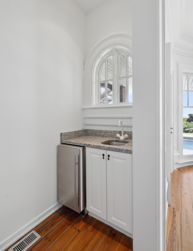 bar with white cabinetry, a healthy amount of sunlight, sink, and dark wood-type flooring