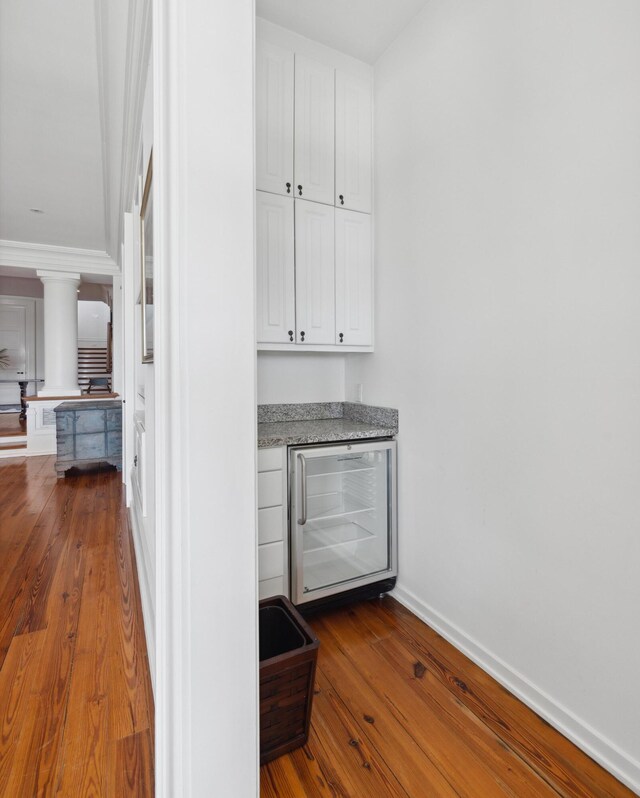 kitchen featuring stone countertops, hardwood / wood-style floors, white cabinets, wine cooler, and ornamental molding