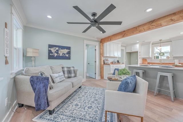 living room with ceiling fan, sink, light wood-type flooring, and crown molding