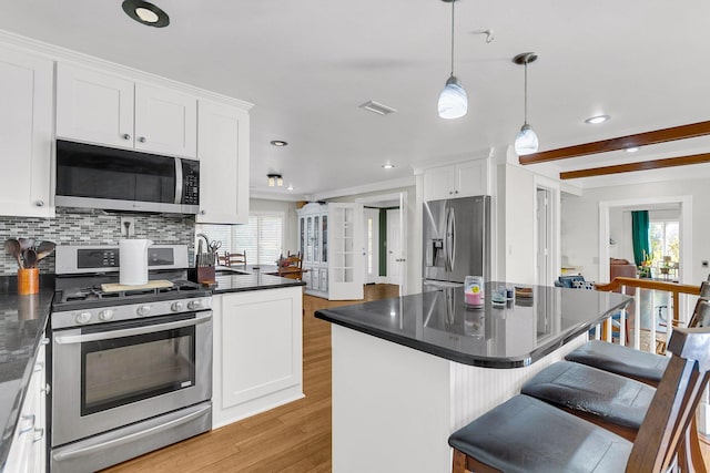 kitchen with a kitchen island, stainless steel appliances, pendant lighting, white cabinets, and light hardwood / wood-style flooring