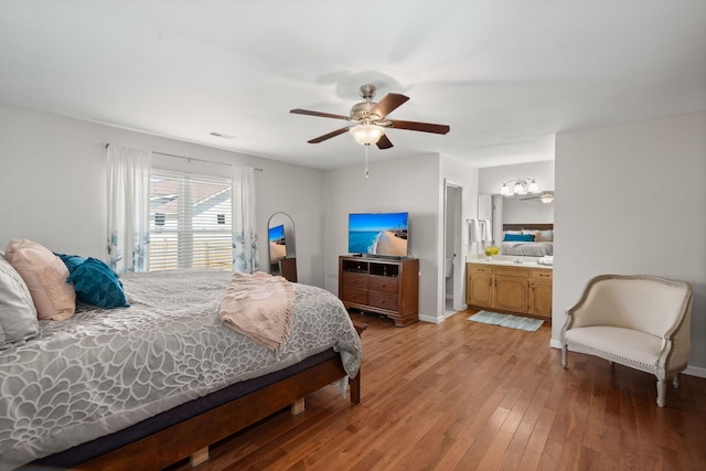 bedroom with connected bathroom, ceiling fan with notable chandelier, and light hardwood / wood-style flooring