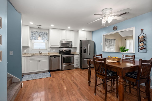 kitchen with sink, decorative light fixtures, stainless steel appliances, light hardwood / wood-style floors, and white cabinets