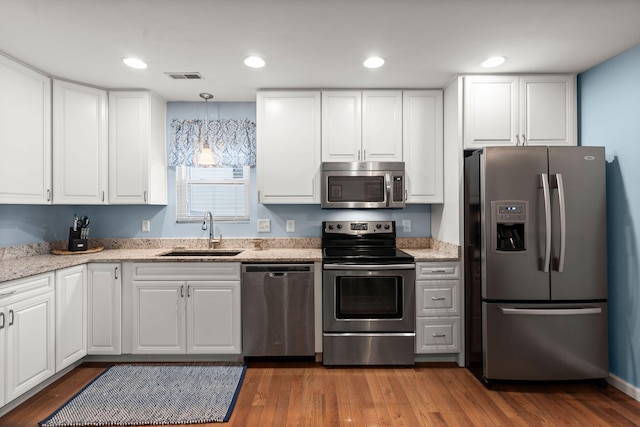 kitchen featuring appliances with stainless steel finishes, pendant lighting, white cabinetry, sink, and light stone countertops