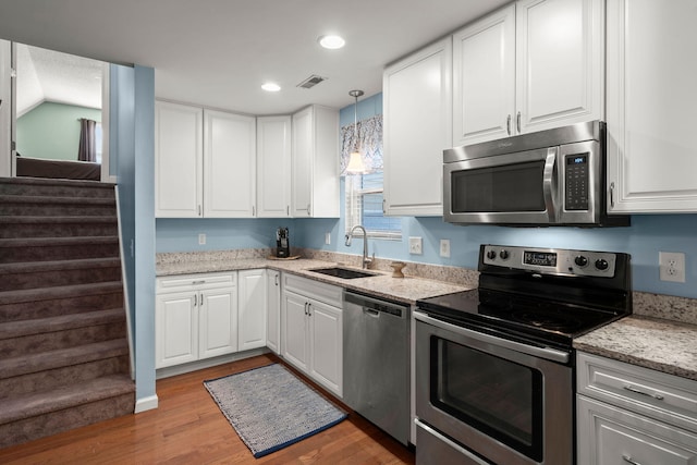 kitchen with sink, white cabinetry, decorative light fixtures, stainless steel appliances, and hardwood / wood-style floors