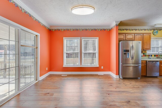 kitchen featuring light wood-type flooring, a sink, appliances with stainless steel finishes, brown cabinetry, and crown molding