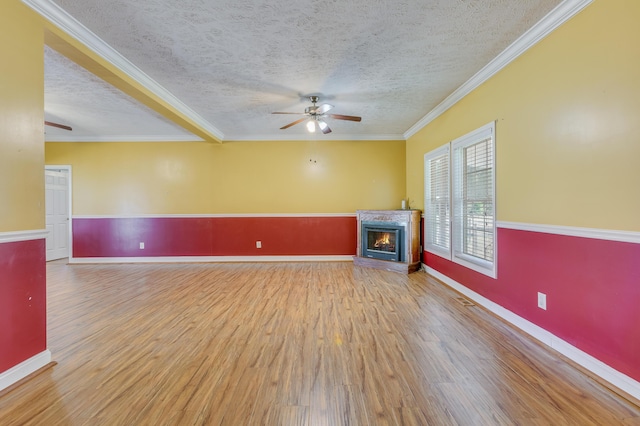 unfurnished living room featuring a ceiling fan, wood finished floors, a lit fireplace, a textured ceiling, and crown molding